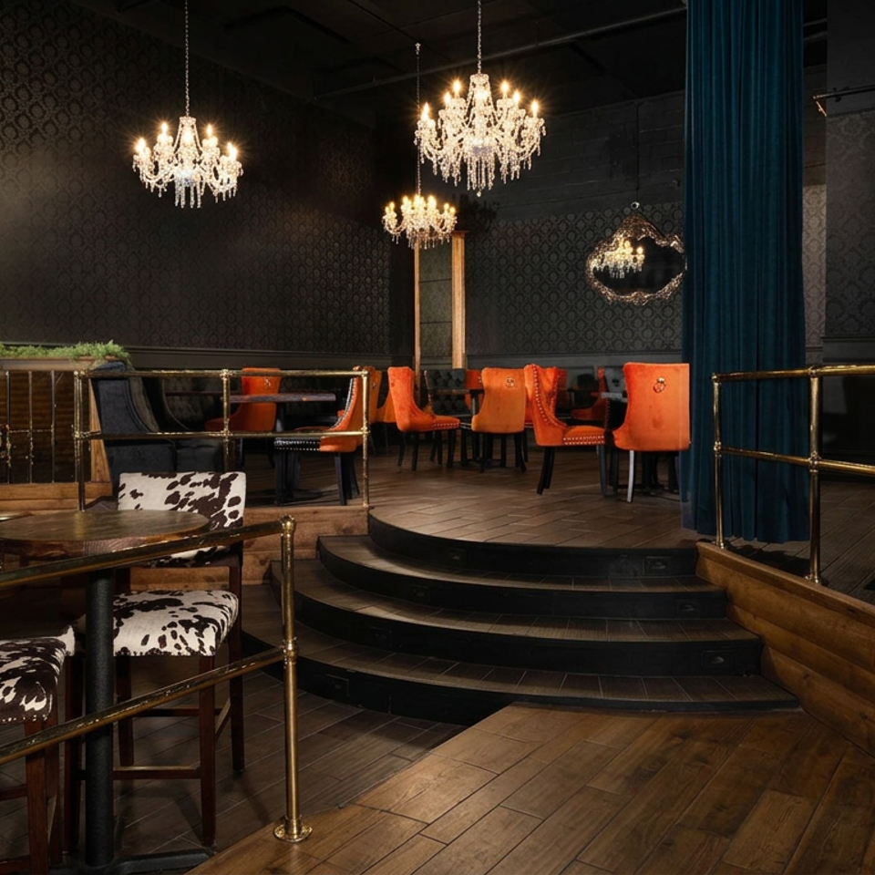 Elegant restaurant lounge with chandeliers, orange dining chairs, cow-print seating, dark blue curtains, and a small raised stage.