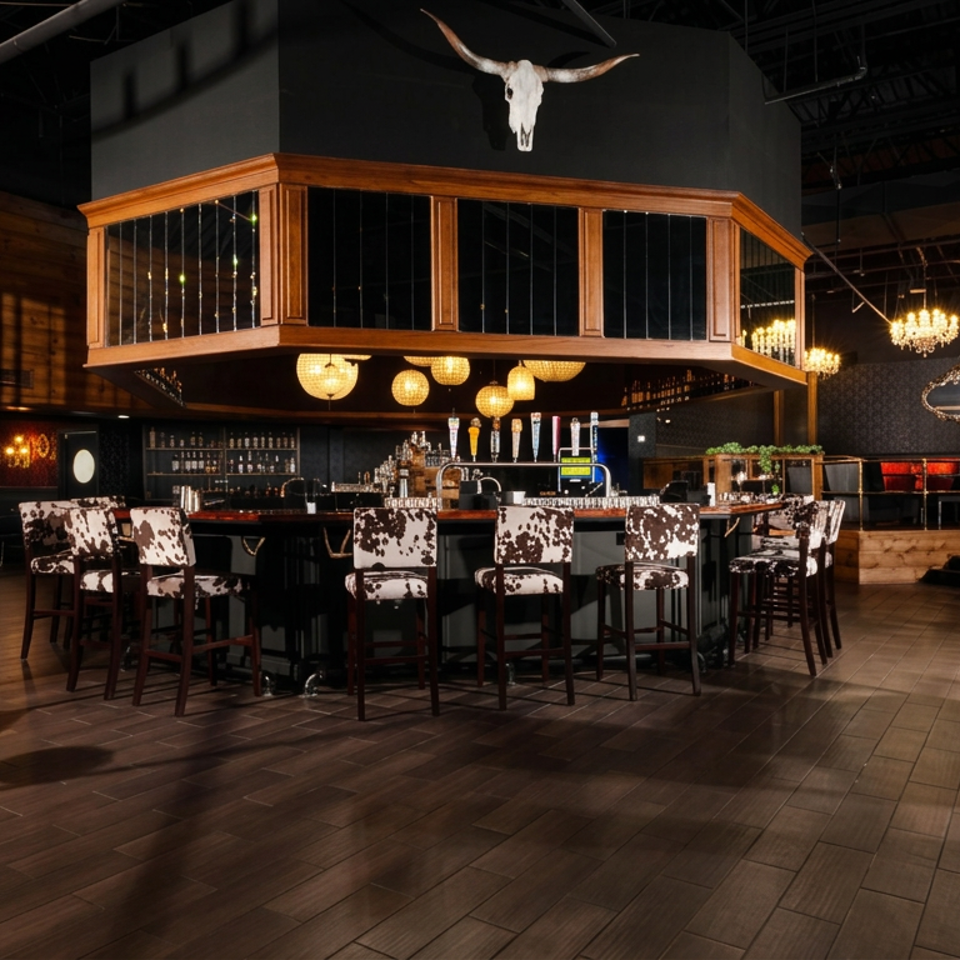 Upscale restaurant bar with cowhide-patterned chairs, chandeliers, dark wood floors, and a longhorn skull mounted above the bar.