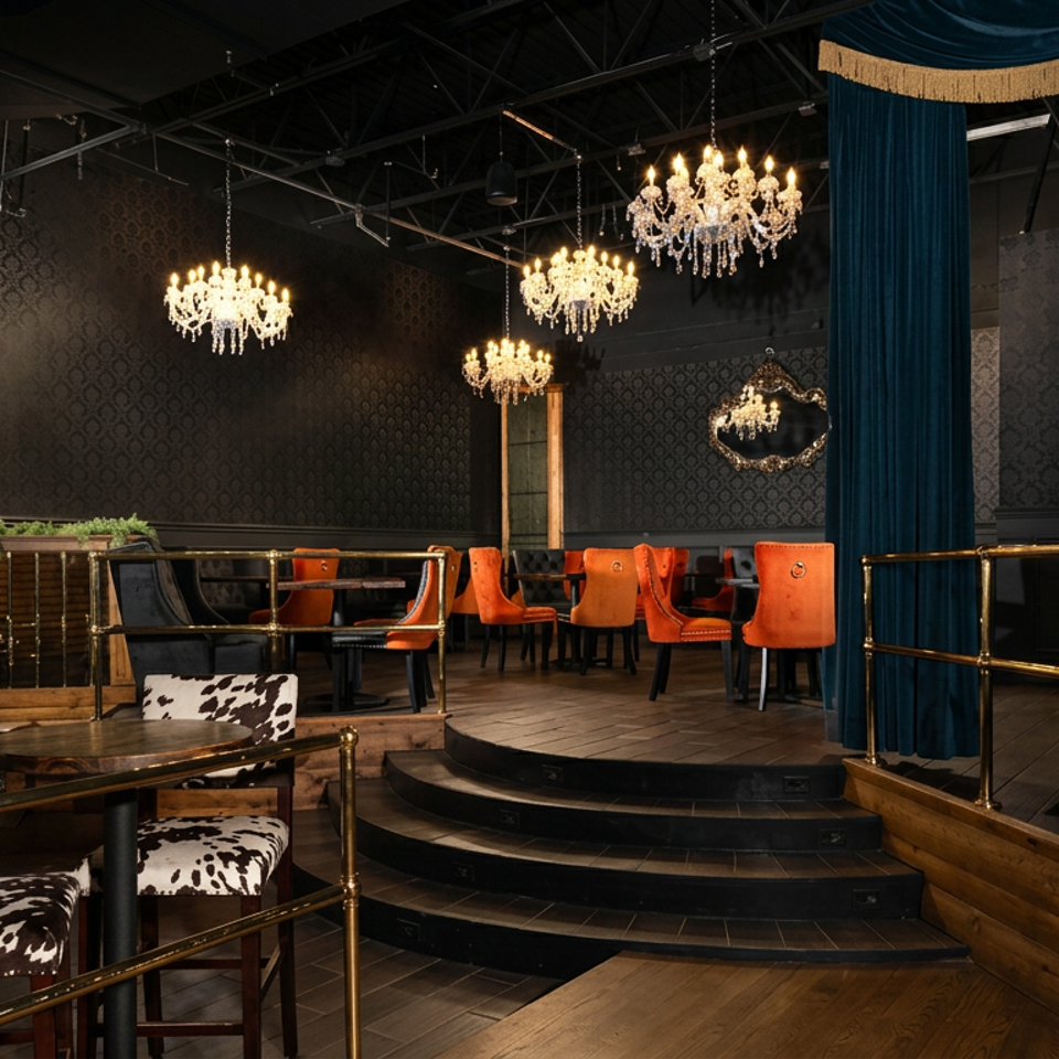 Elegant restaurant interior with chandeliers, patterned walls, orange chairs, cowhide seating, and a small curtained stage.