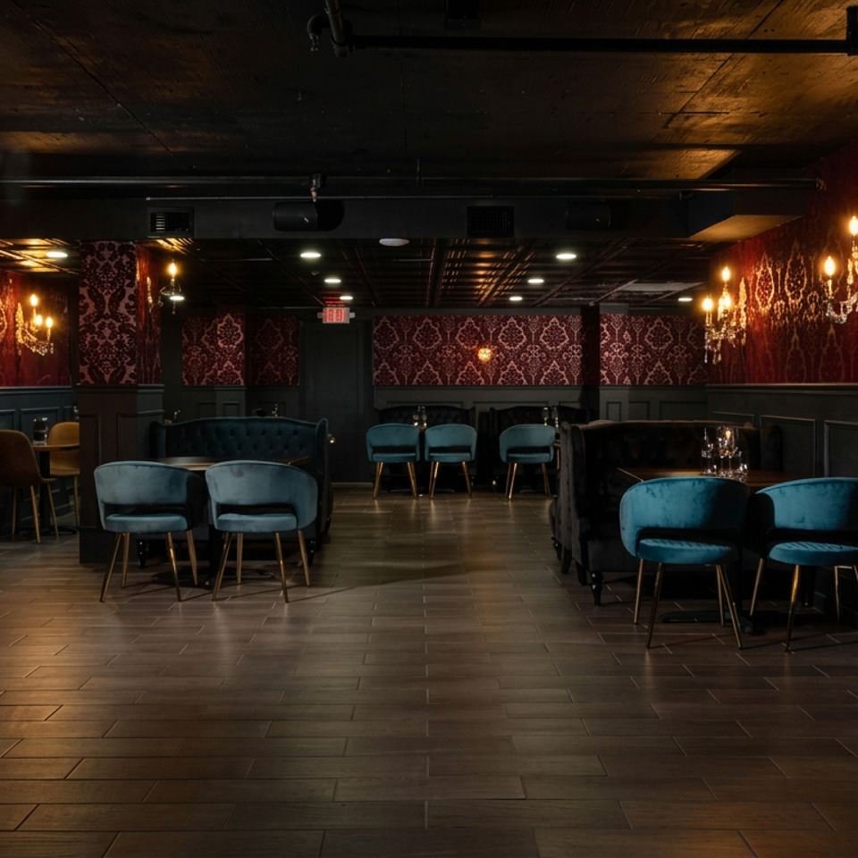 Elegant lounge restaurant interior with teal velvet chairs, dark banquettes, red patterned wallpaper, chandeliers, and warm ambient lighting.