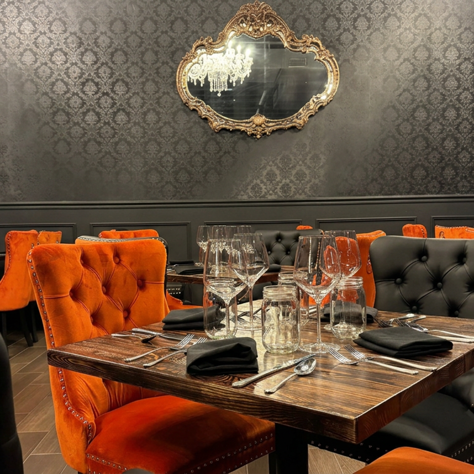 Elegant restaurant dining room with orange and black tufted chairs, set tables, patterned walls, and ornate mirrors.